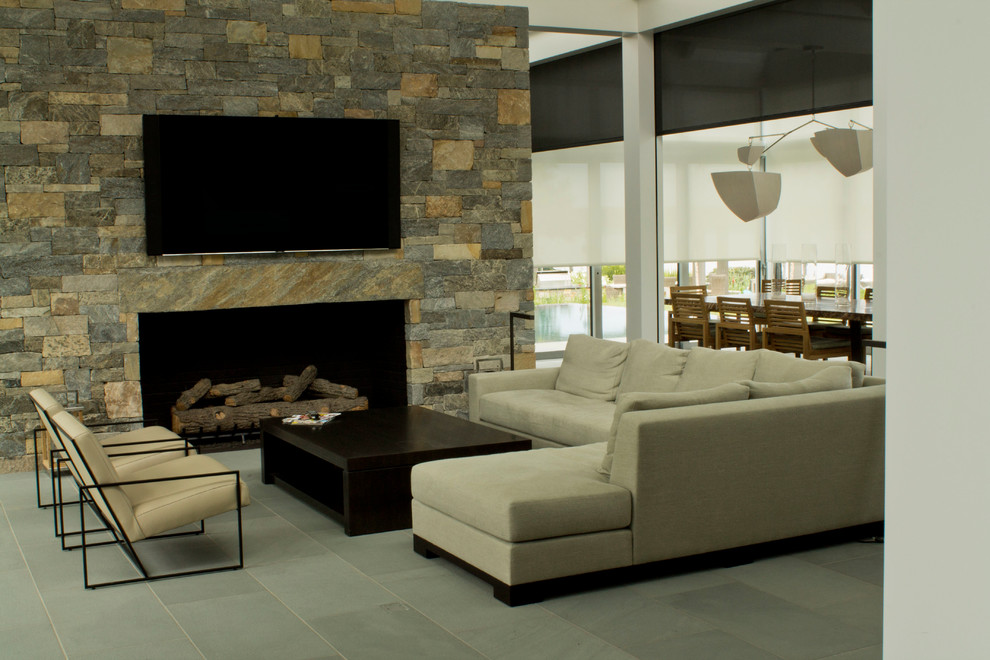 Imagen de salón abierto actual de tamaño medio con marco de chimenea de piedra, televisor colgado en la pared, paredes beige, suelo de pizarra, todas las chimeneas y suelo gris