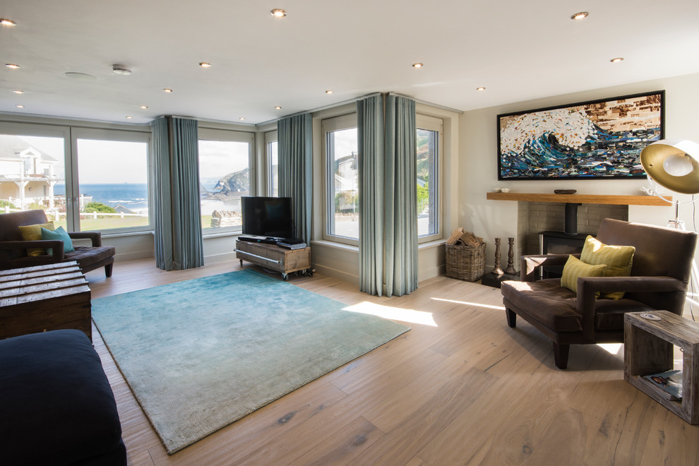 Пример оригинального дизайна: гостиная комната в морском стиле с бежевыми стенами, светлым паркетным полом, отдельно стоящим телевизором и синими шторами