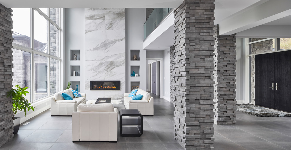 На фото: огромная парадная, открытая гостиная комната в стиле модернизм с серыми стенами, полом из сланца, горизонтальным камином, фасадом камина из камня и серым полом без телевизора с