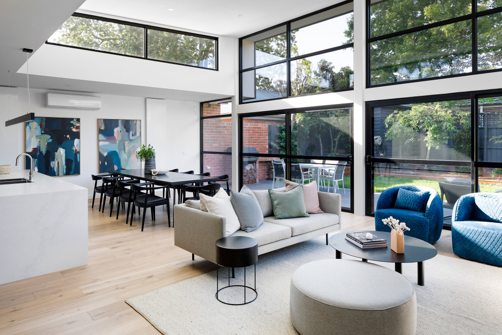 Mittelgroßes, Offenes Modernes Wohnzimmer mit weißer Wandfarbe, hellem Holzboden, Kamin, verputzter Kaminumrandung, TV-Wand und braunem Boden in Melbourne