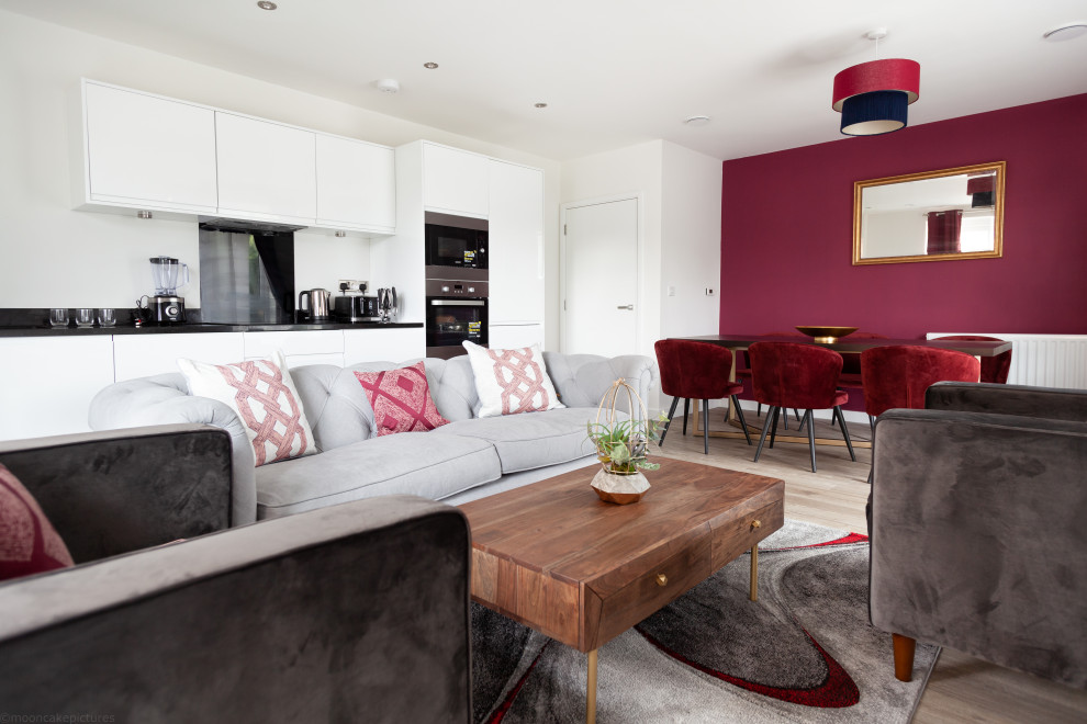 This is an example of a medium sized modern formal open plan living room in London with a wall mounted tv, red walls, light hardwood flooring, no fireplace and brown floors.