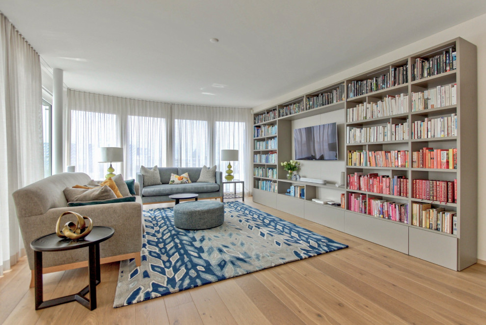 Ejemplo de biblioteca en casa actual con paredes blancas, suelo de madera clara, pared multimedia y suelo beige
