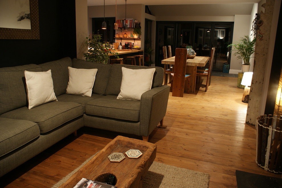 Modelo de salón abierto actual de tamaño medio con paredes negras, suelo de madera oscura, estufa de leña, marco de chimenea de ladrillo y televisor independiente