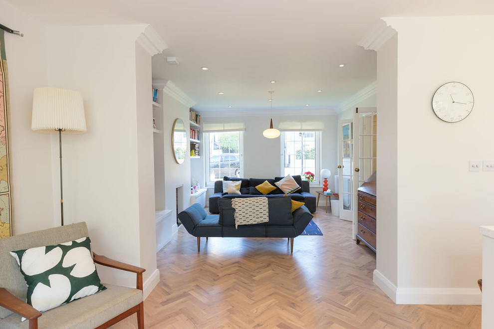 Example of a mid-sized trendy open concept light wood floor and brown floor living room library design in London with white walls, a standard fireplace and no tv