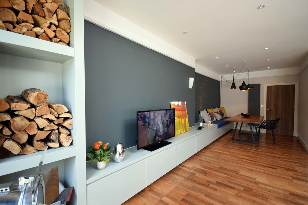 Modelo de salón para visitas abierto actual grande con paredes grises, estufa de leña, suelo laminado, televisor independiente y suelo marrón