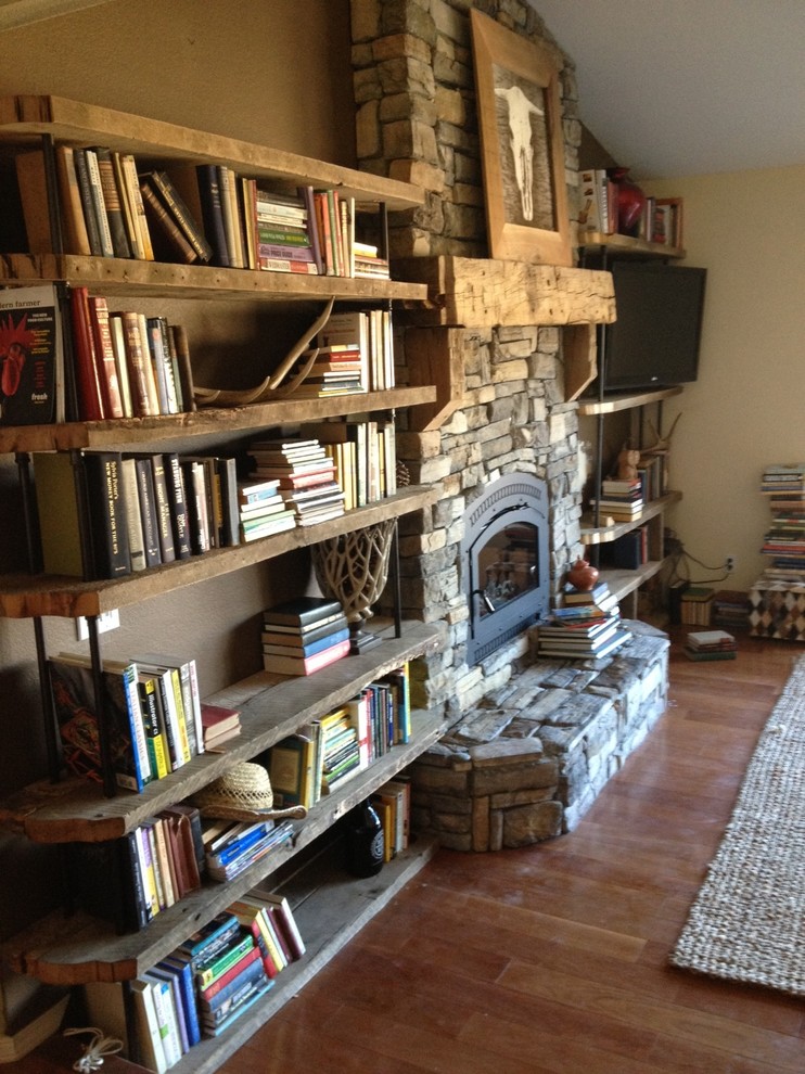 Inspiration for a small rustic living room library remodel in San Luis Obispo with a wood stove, a stone fireplace and a wall-mounted tv