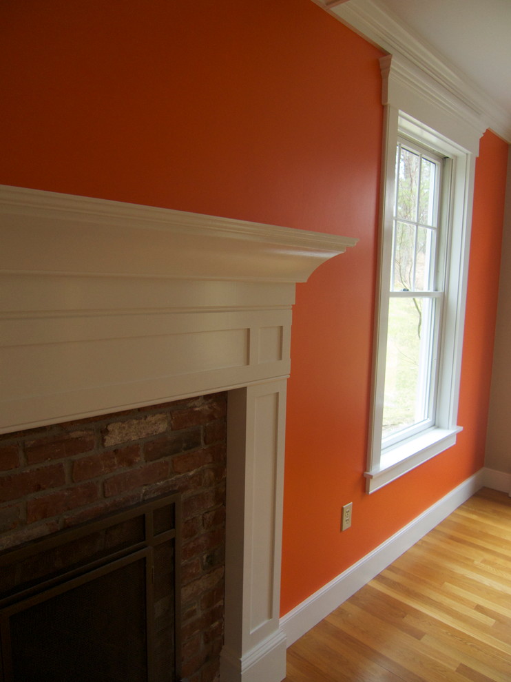 ボストンにある高級な小さなコンテンポラリースタイルのおしゃれなリビング (オレンジの壁、淡色無垢フローリング、標準型暖炉、木材の暖炉まわり、テレビなし、ベージュの床) の写真