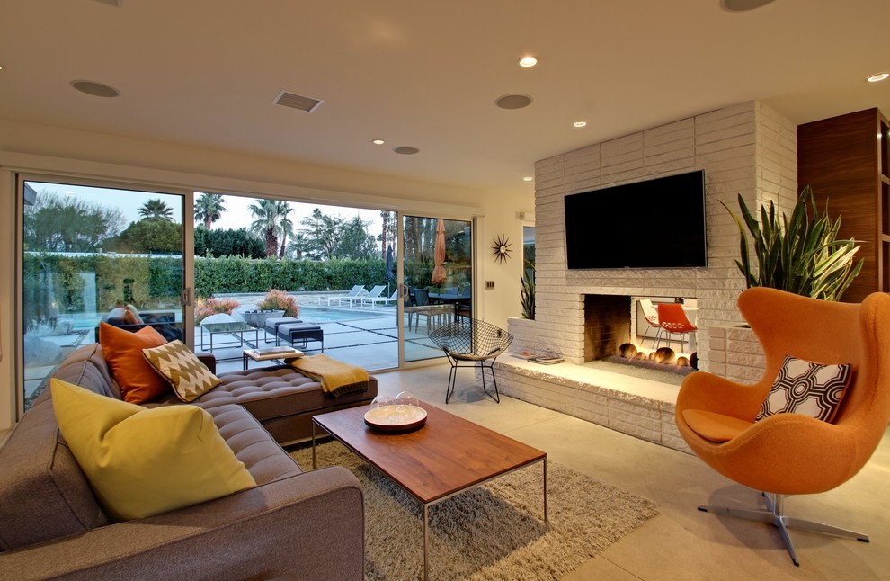 Пример оригинального дизайна: открытая гостиная комната среднего размера в современном стиле с белыми стенами, бетонным полом, двусторонним камином, фасадом камина из кирпича и телевизором на стене