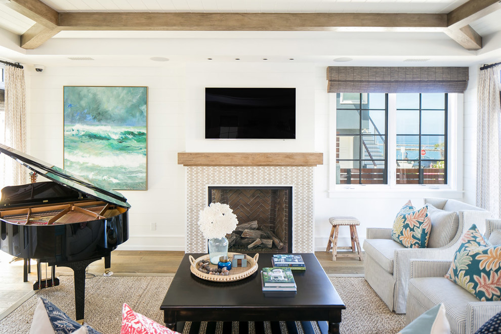 Example of a large island style open concept medium tone wood floor and brown floor living room design in Orange County with white walls, a standard fireplace, a tile fireplace and a wall-mounted tv