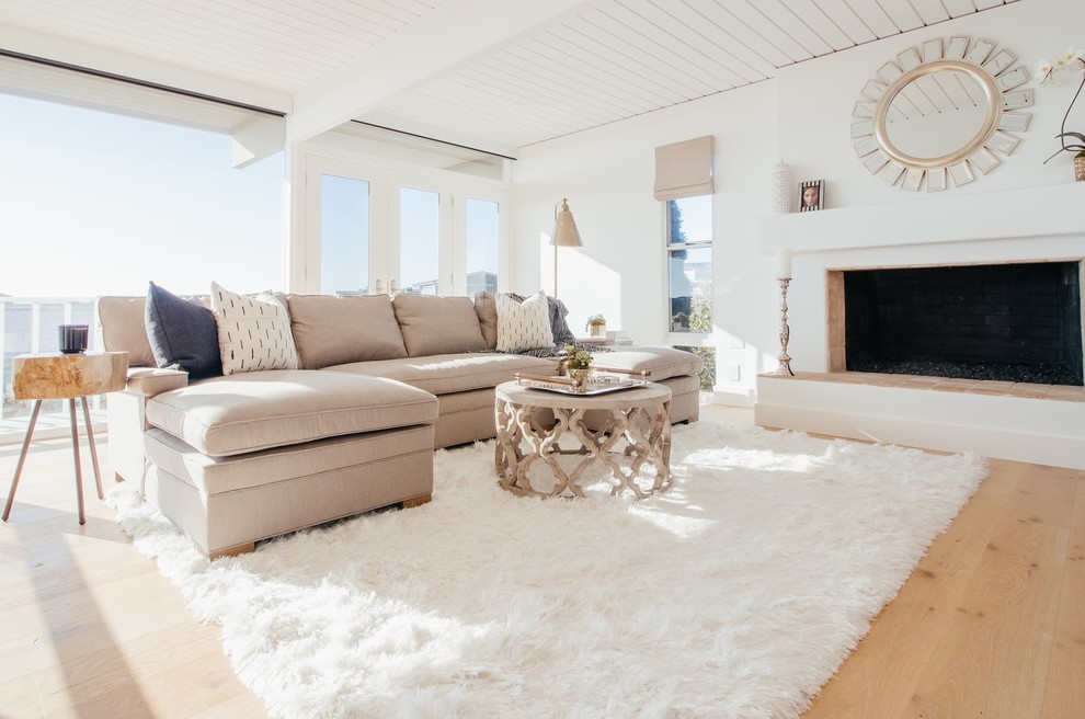 Example of a large beach style formal and open concept light wood floor and brown floor living room design in Orange County with white walls, a standard fireplace, a plaster fireplace and no tv