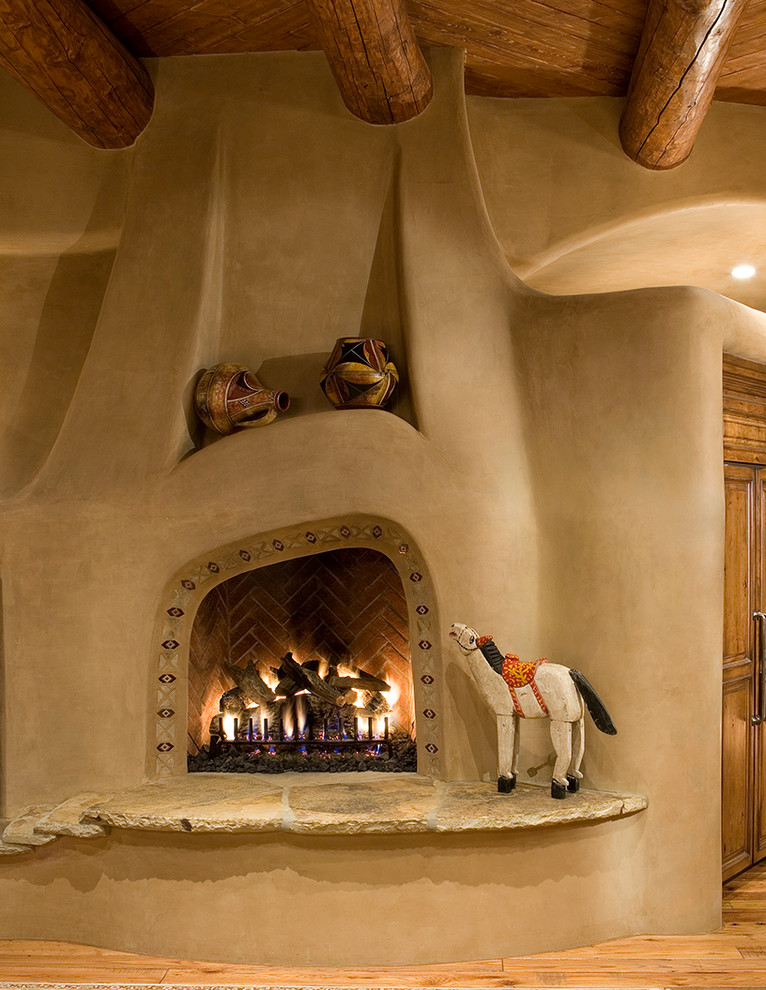 フェニックスにあるラグジュアリーなサンタフェスタイルのおしゃれなリビング (ベージュの壁、標準型暖炉、漆喰の暖炉まわり、無垢フローリング) の写真