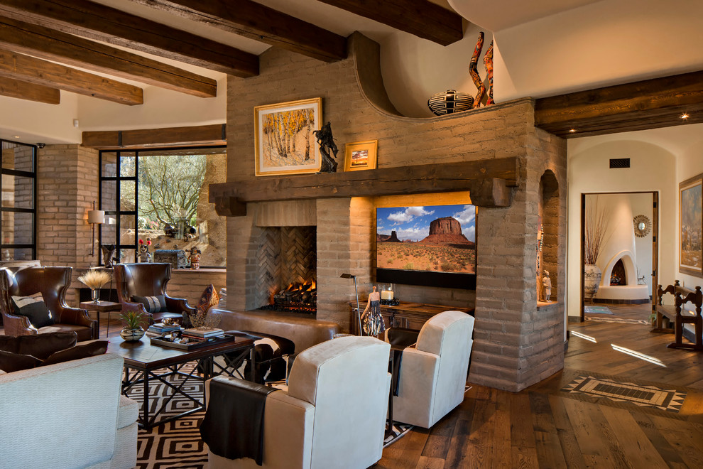 Idée de décoration pour un grand salon sud-ouest américain ouvert avec une salle de réception, un mur beige, un sol en bois brun, une cheminée standard, un manteau de cheminée en pierre, un téléviseur encastré et un sol marron.