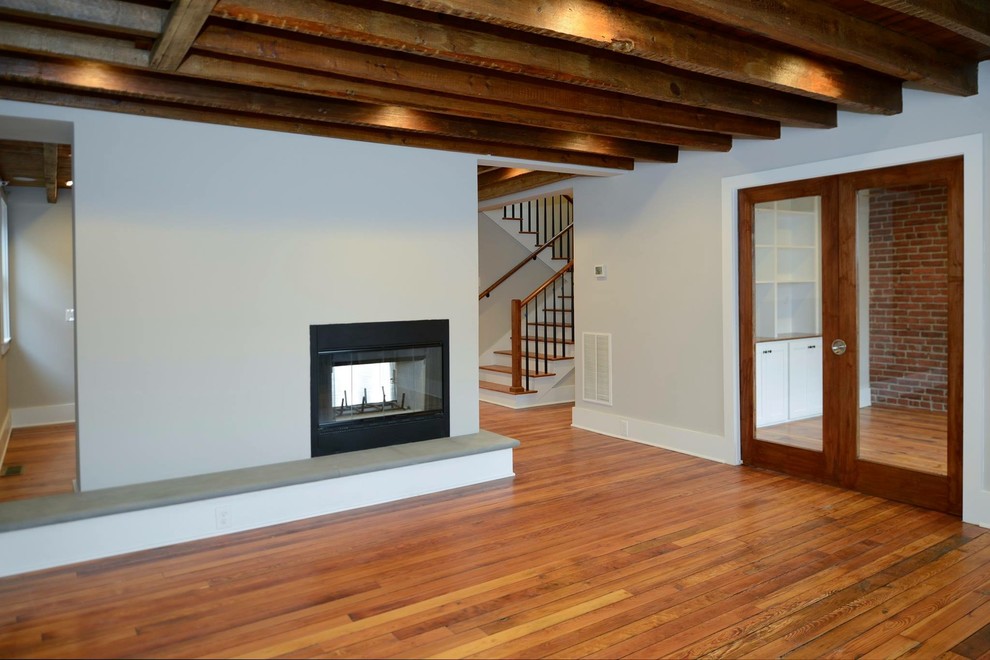 Cette image montre un salon chalet de taille moyenne et ouvert avec un mur gris, un sol en bois brun, une cheminée double-face, un téléviseur dissimulé et un sol marron.