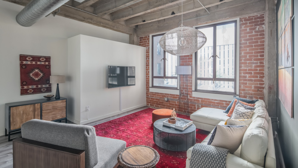 This is an example of an urban open plan living room in Phoenix with grey walls, dark hardwood flooring, a wall mounted tv, grey floors and brick walls.