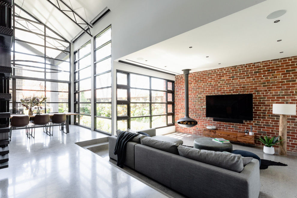 Immagine di un soggiorno industriale aperto con pareti bianche, pavimento in cemento, camino sospeso, TV a parete, pavimento grigio e pareti in mattoni