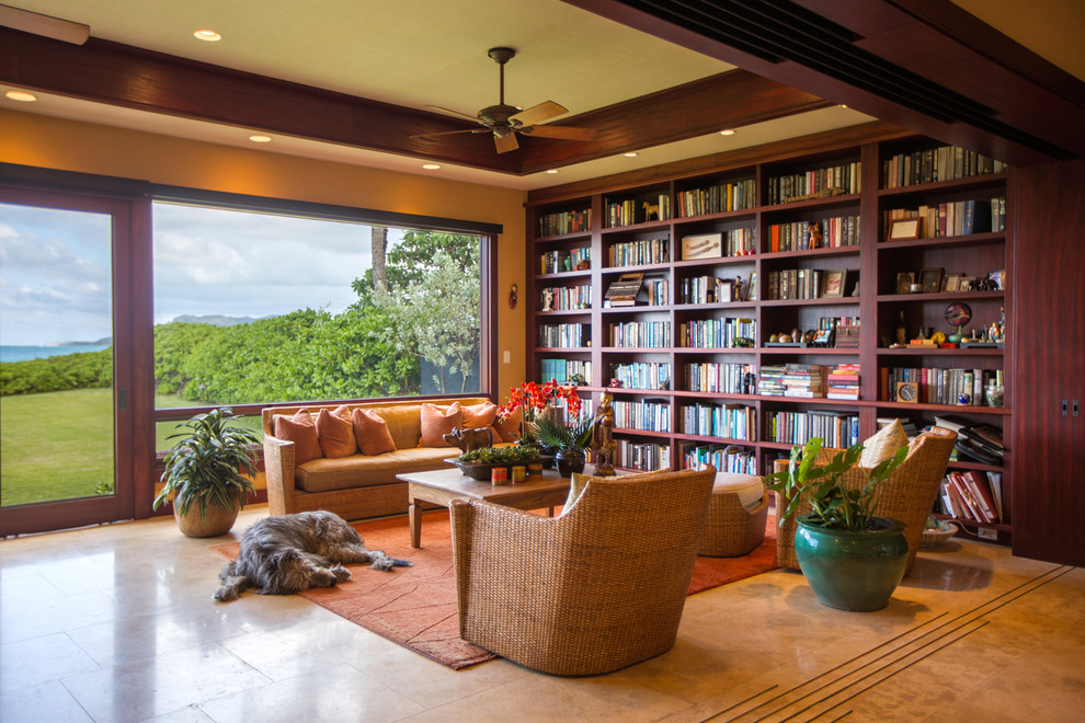 Modelo de biblioteca en casa abierta tropical de tamaño medio sin chimenea con paredes beige, suelo de baldosas de porcelana y suelo beige