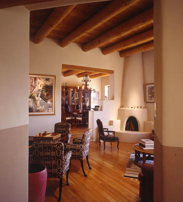Exemple d'un salon sud-ouest américain de taille moyenne et ouvert avec une salle de réception, un mur beige, un sol en bois brun, une cheminée standard, un manteau de cheminée en plâtre, aucun téléviseur et un sol marron.
