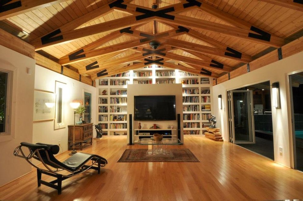 Foto di un grande soggiorno tropicale con libreria, pareti bianche, pavimento in legno massello medio, nessun camino e TV a parete