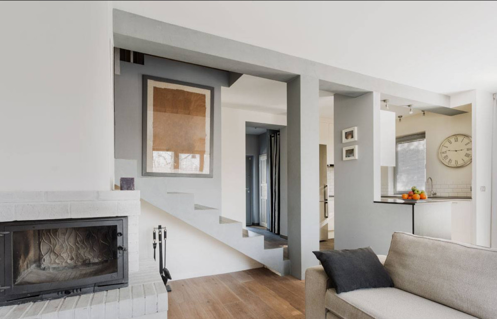 Cette image montre un salon minimaliste de taille moyenne et ouvert avec une salle de réception, un mur gris, un sol en bois brun, une cheminée standard, un manteau de cheminée en brique et aucun téléviseur.