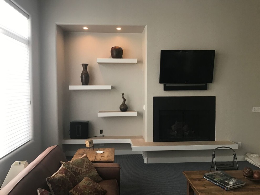 Cette image montre un salon design de taille moyenne et fermé avec un mur beige, moquette, une cheminée standard, un manteau de cheminée en plâtre, un téléviseur fixé au mur et un sol gris.