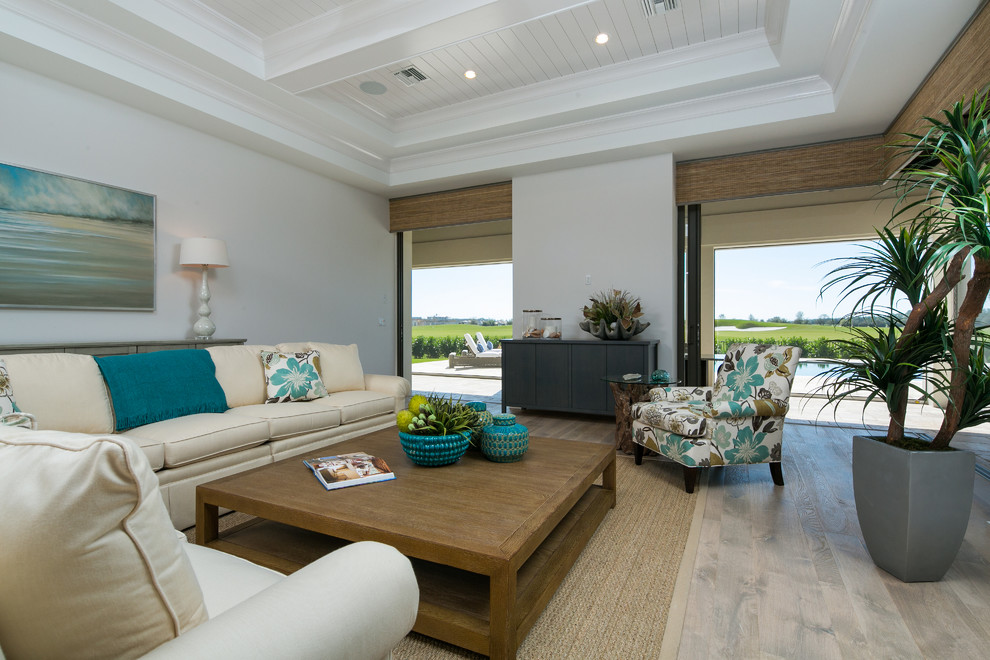 Foto de salón para visitas abierto tropical grande sin chimenea y televisor con paredes blancas y suelo de madera clara