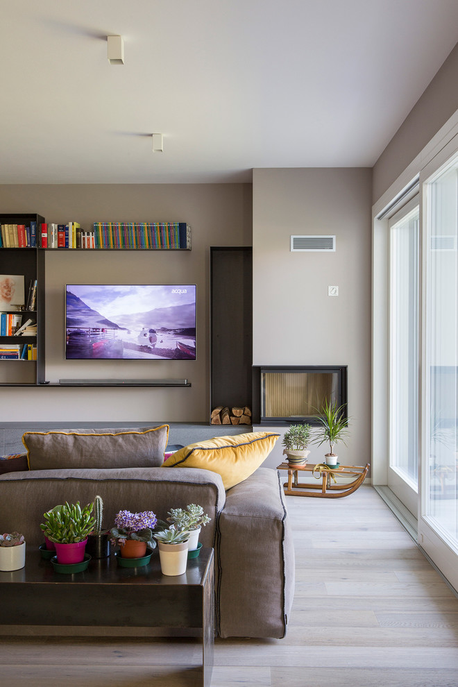 Ejemplo de salón actual con paredes beige, suelo de madera clara, chimenea de doble cara, televisor colgado en la pared y suelo beige