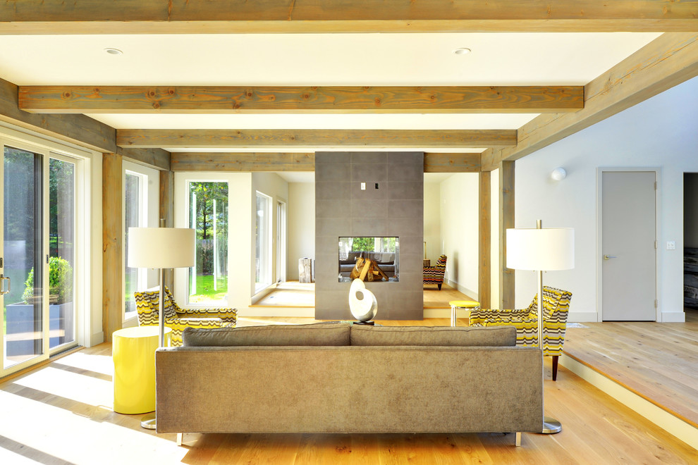 Стильный дизайн: большая открытая гостиная комната в современном стиле с двусторонним камином, серыми стенами, светлым паркетным полом и фасадом камина из бетона - последний тренд