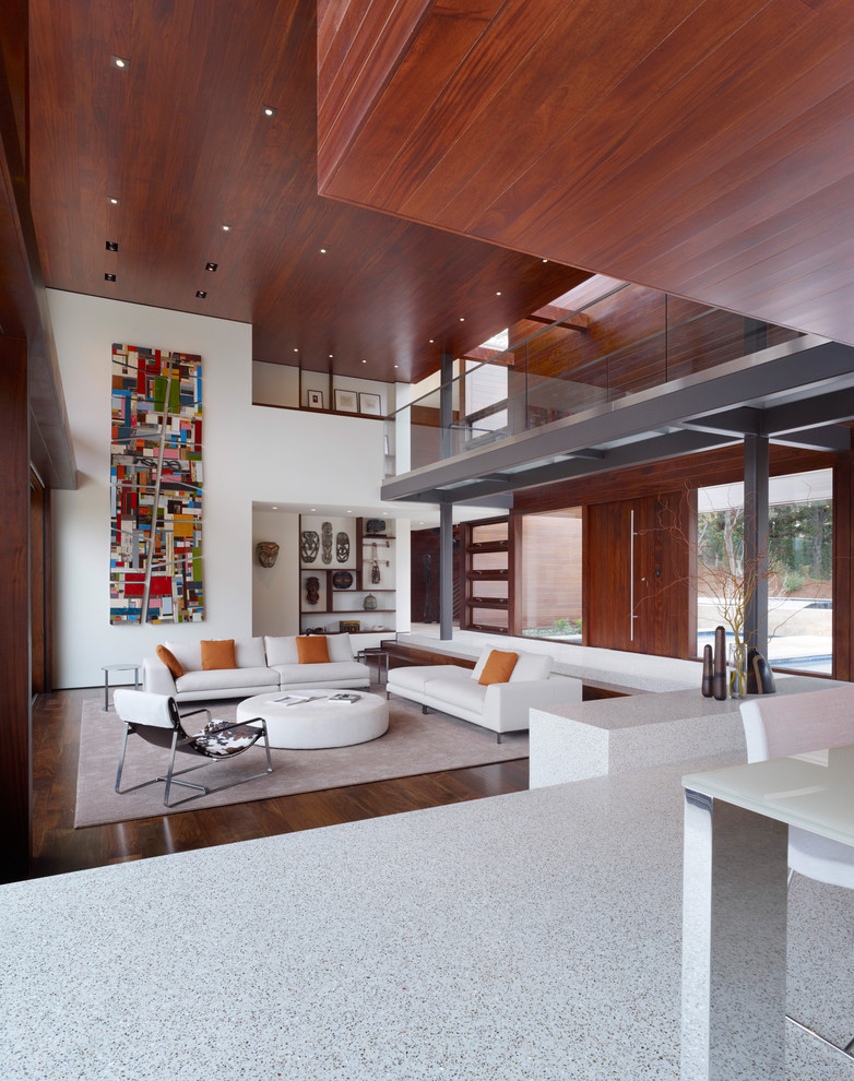 На фото: большая открытая гостиная комната в стиле модернизм с белыми стенами, темным паркетным полом и ковром на полу с