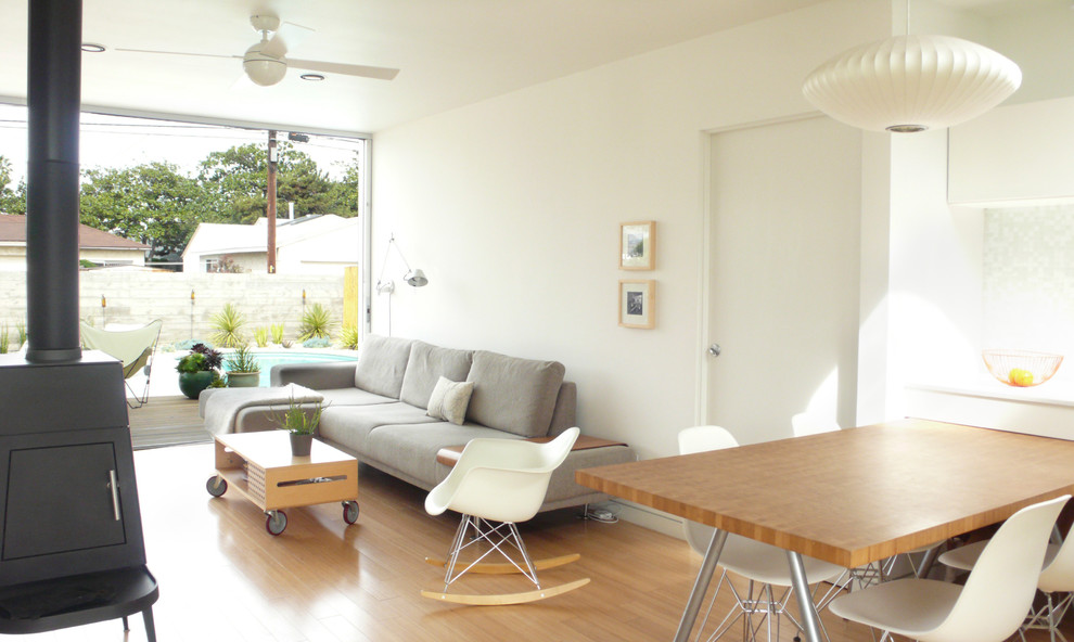 Living room - small modern open concept medium tone wood floor living room idea in Los Angeles with white walls and a wood stove