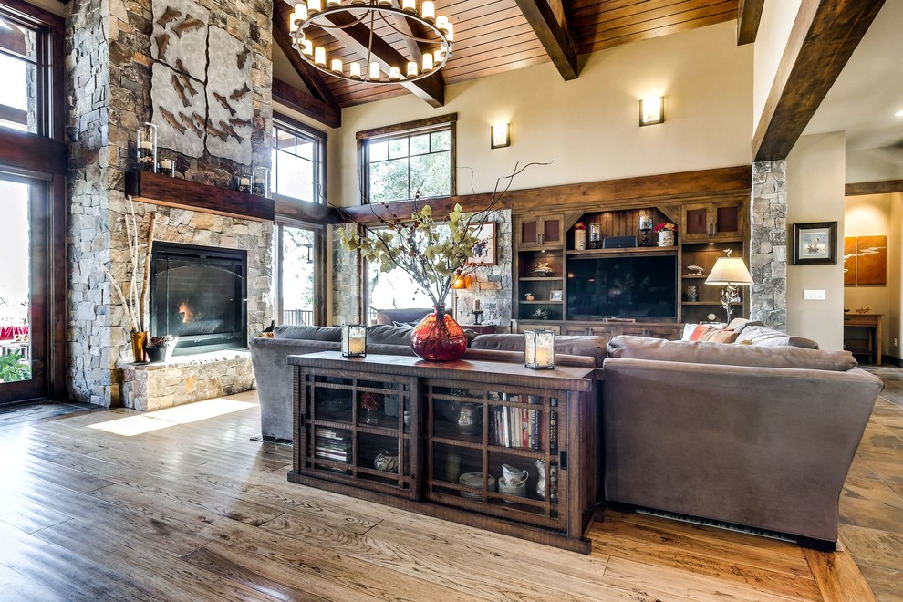 Example of a mid-sized mountain style formal and open concept medium tone wood floor and brown floor living room design in Sacramento with beige walls, a standard fireplace, a stone fireplace and a media wall