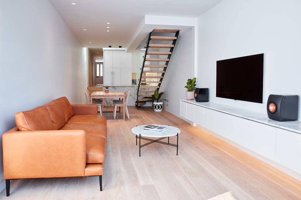 Modelo de salón abierto contemporáneo con paredes blancas, suelo de madera clara, televisor colgado en la pared y suelo beige