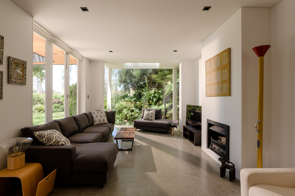 This is an example of a beach style living room in Sydney with white walls, concrete flooring, a standard fireplace and grey floors.