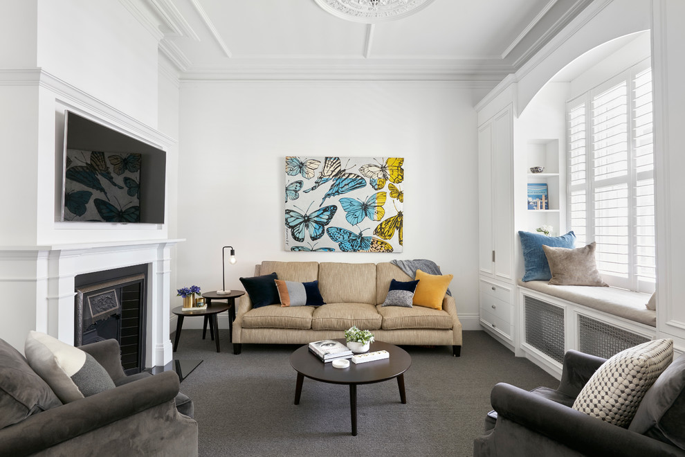 На фото: гостиная комната в стиле неоклассика (современная классика) с белыми стенами, ковровым покрытием, стандартным камином, телевизором на стене и серым полом