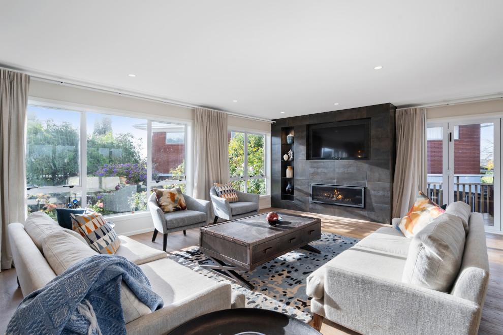 Mittelgroßes, Offenes Klassisches Wohnzimmer mit braunem Holzboden, gefliester Kaminumrandung, TV-Wand, beiger Wandfarbe, Gaskamin und braunem Boden in Auckland
