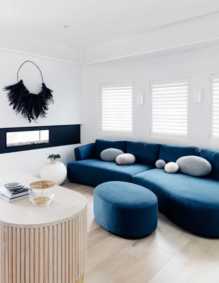 シドニーにあるビーチスタイルのおしゃれなリビング (白い壁、淡色無垢フローリング、両方向型暖炉、テレビなし、ベージュの床、青いソファ) の写真