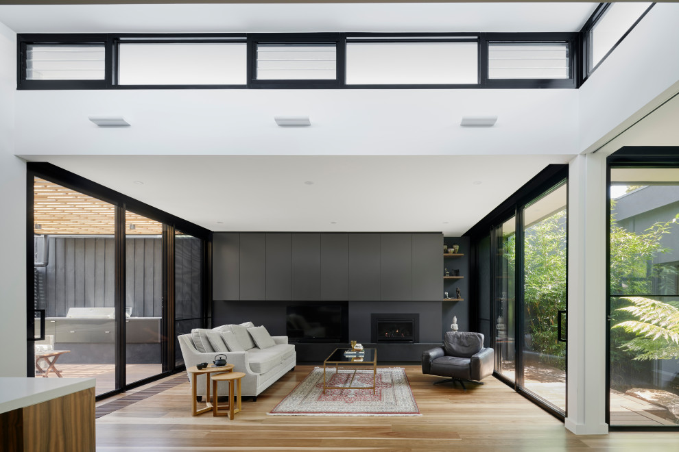 Großes, Offenes Modernes Wohnzimmer mit weißer Wandfarbe, braunem Holzboden, Kamin, Kaminumrandung aus Metall, TV-Wand und beigem Boden in Melbourne