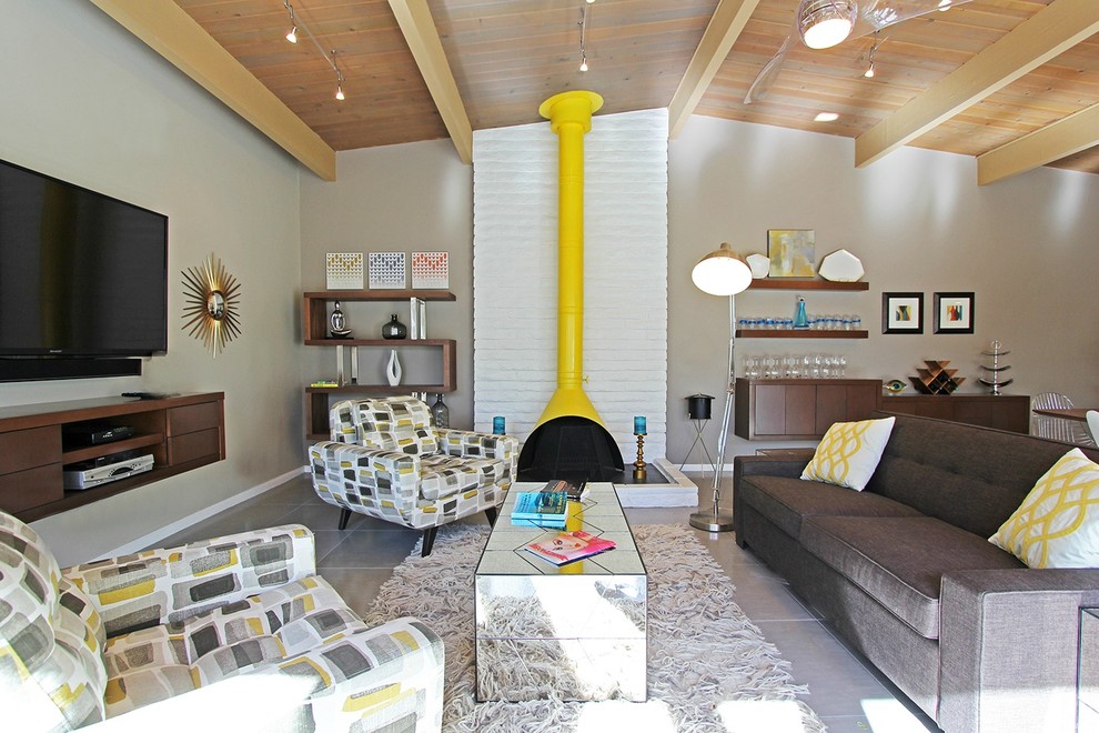 Modelo de salón abierto vintage grande con paredes beige, suelo de baldosas de cerámica, estufa de leña, marco de chimenea de ladrillo, televisor colgado en la pared y suelo gris