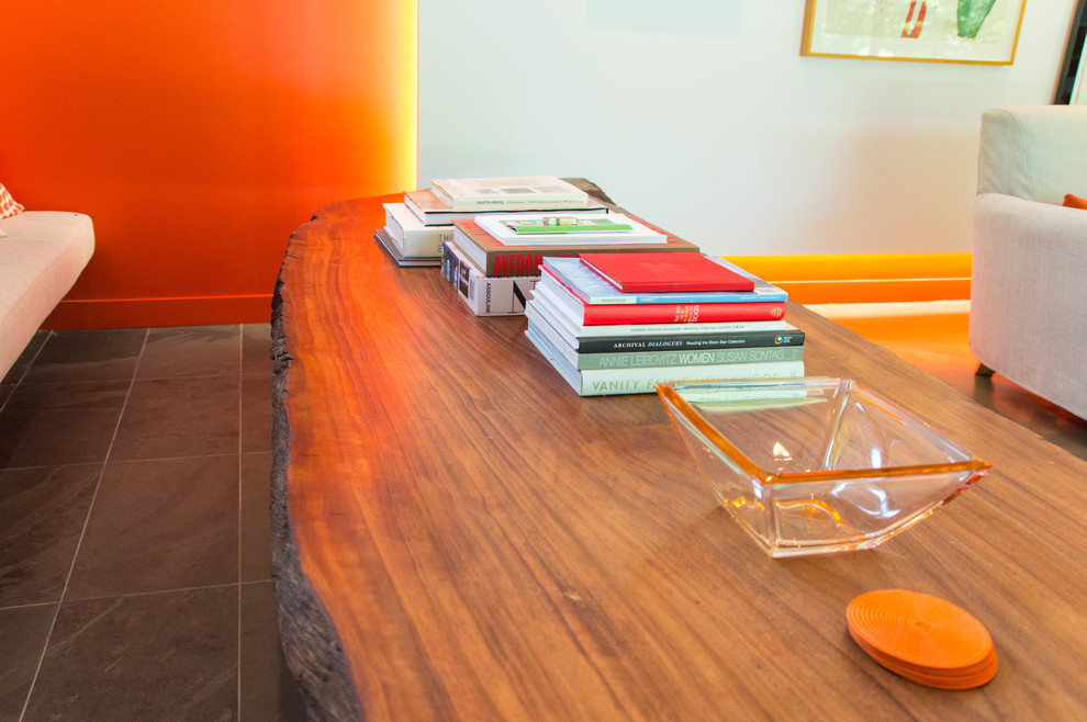 На фото: огромная открытая гостиная комната в стиле модернизм с с книжными шкафами и полками, оранжевыми стенами, полом из керамической плитки и серым полом