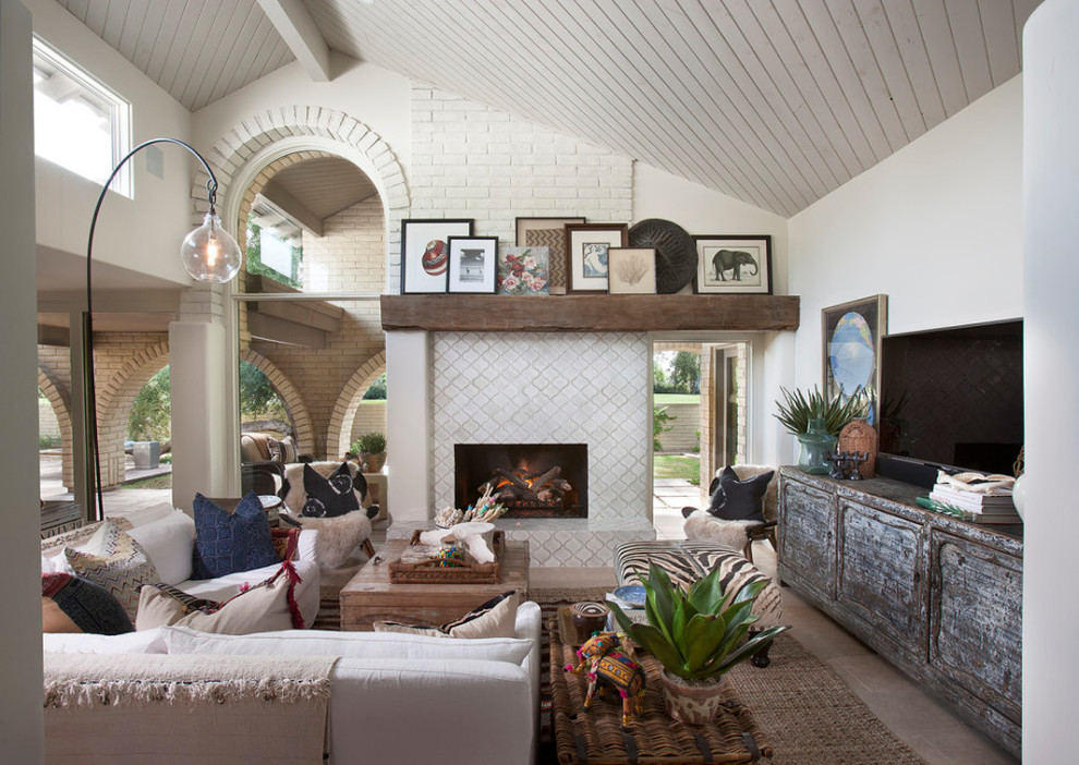Exemple d'un grand salon chic ouvert avec un mur blanc, un sol en calcaire, une cheminée standard, un manteau de cheminée en brique, un téléviseur indépendant et un sol beige.