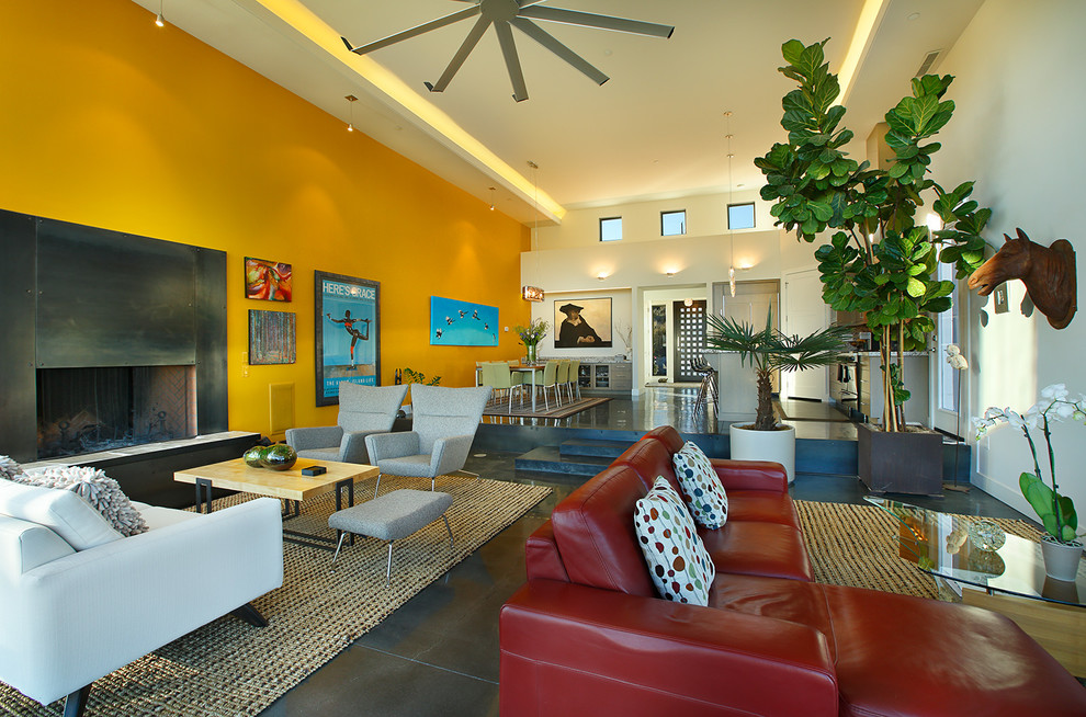 Immagine di un soggiorno design di medie dimensioni e aperto con pareti gialle, pavimento in cemento, camino classico, cornice del camino in metallo, TV a parete e pavimento marrone