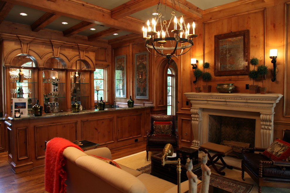 Example of a large tuscan enclosed medium tone wood floor, brown floor, exposed beam and wall paneling living room design in Dallas with a bar, brown walls, a standard fireplace, a stone fireplace and no tv