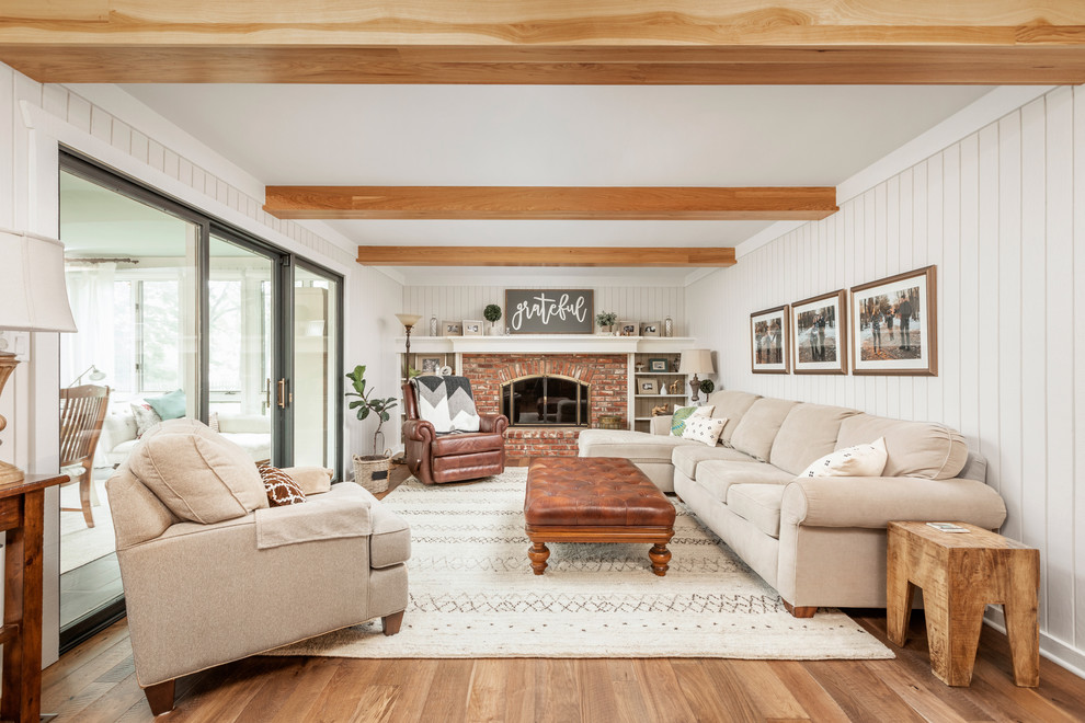 Landhausstil Wohnzimmer mit weißer Wandfarbe, braunem Holzboden, Kamin, Kaminumrandung aus Backstein und braunem Boden in Indianapolis