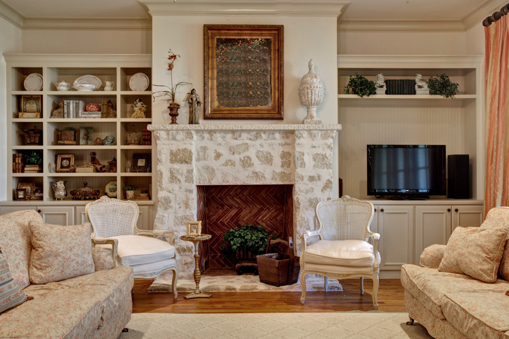 Cette image montre un salon traditionnel de taille moyenne avec une salle de réception, un mur blanc, un sol en bois brun, une cheminée standard, un manteau de cheminée en pierre et un téléviseur encastré.