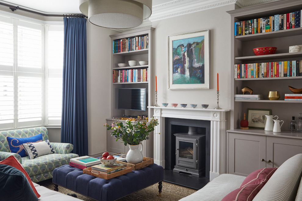 Стильный дизайн: изолированная гостиная комната в стиле неоклассика (современная классика) с серыми стенами, печью-буржуйкой, телевизором на стене и синими шторами - последний тренд