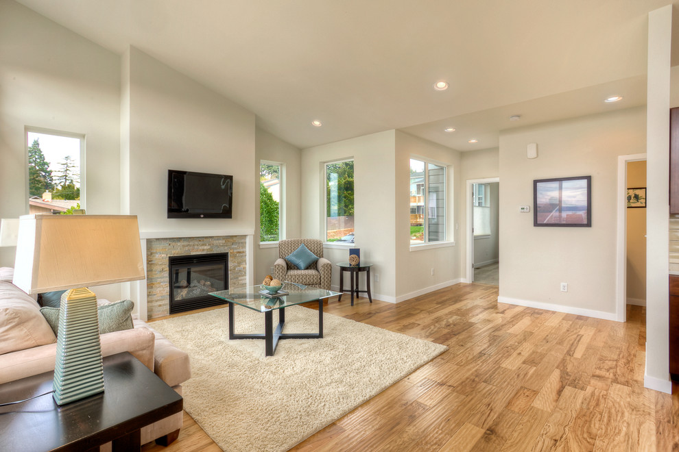 Mittelgroßes, Offenes Modernes Wohnzimmer mit weißer Wandfarbe, hellem Holzboden, Kamin, Kaminumrandung aus Stein und TV-Wand in Seattle