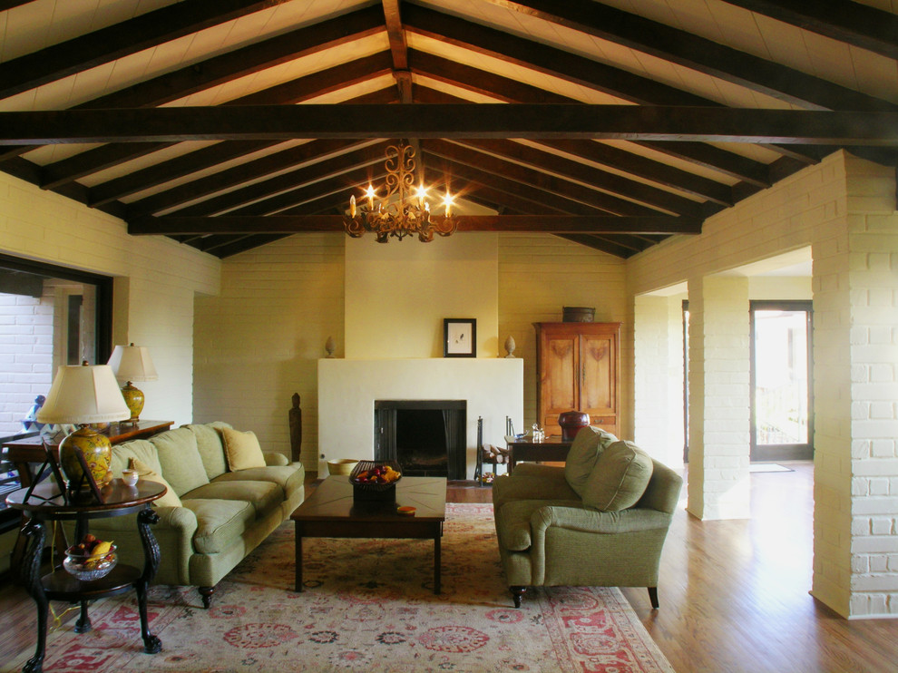 Aménagement d'un grand salon méditerranéen avec un mur beige, un sol en bois brun, une cheminée standard et un manteau de cheminée en plâtre.