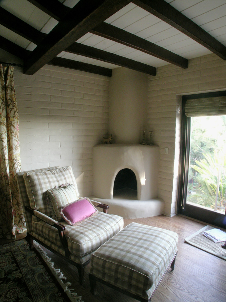 Aménagement d'un grand salon méditerranéen avec un mur blanc, un sol en bois brun, une cheminée d'angle et un manteau de cheminée en plâtre.