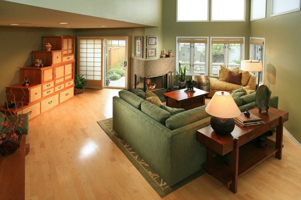 Exemple d'un petit salon craftsman ouvert avec un mur vert, parquet clair, une cheminée double-face et un manteau de cheminée en pierre.