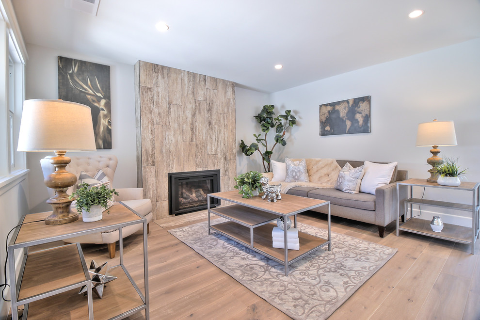 Idee per un soggiorno minimalista aperto con pareti grigie, parquet chiaro, camino classico, cornice del camino piastrellata e pavimento grigio