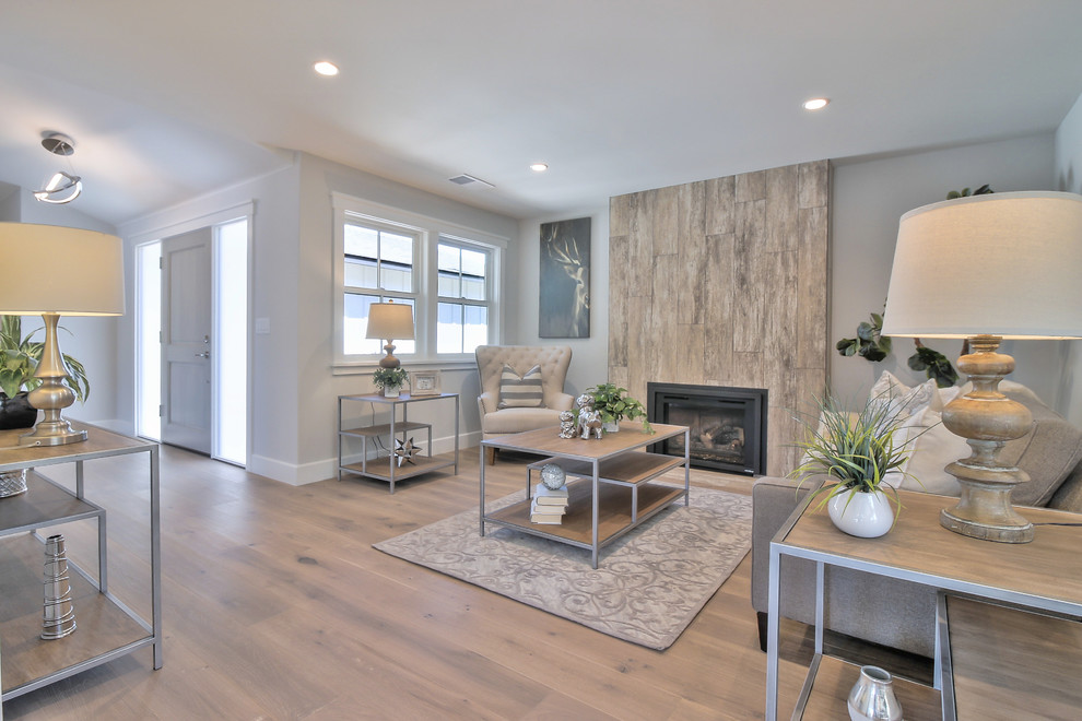 Cette image montre un salon minimaliste ouvert avec un mur gris, parquet clair, une cheminée standard, un manteau de cheminée en carrelage et un sol gris.